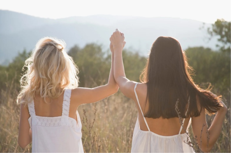 Duas mulheres de mãos dadas em campo aberto, simbolizando acolhimento e bem-estar na saúde da mulher
